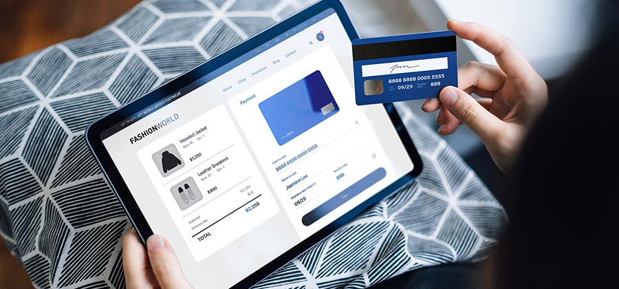 Person making an online purchase using a tablet and a credit card, displaying a checkout page from a fashion e-commerce site with product details and payment information.